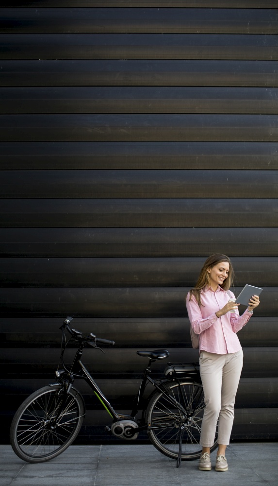 Young woman with tablet and e-bike outdoor on sunny day