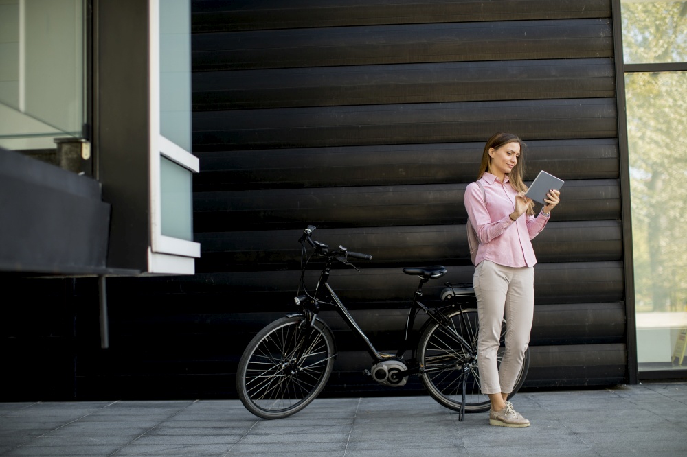 Happy young woman with files in the hands standing outdoor next to electric bike