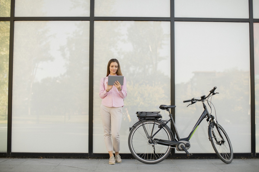 Young woman with tablet and e-bike outdoor on sunny day