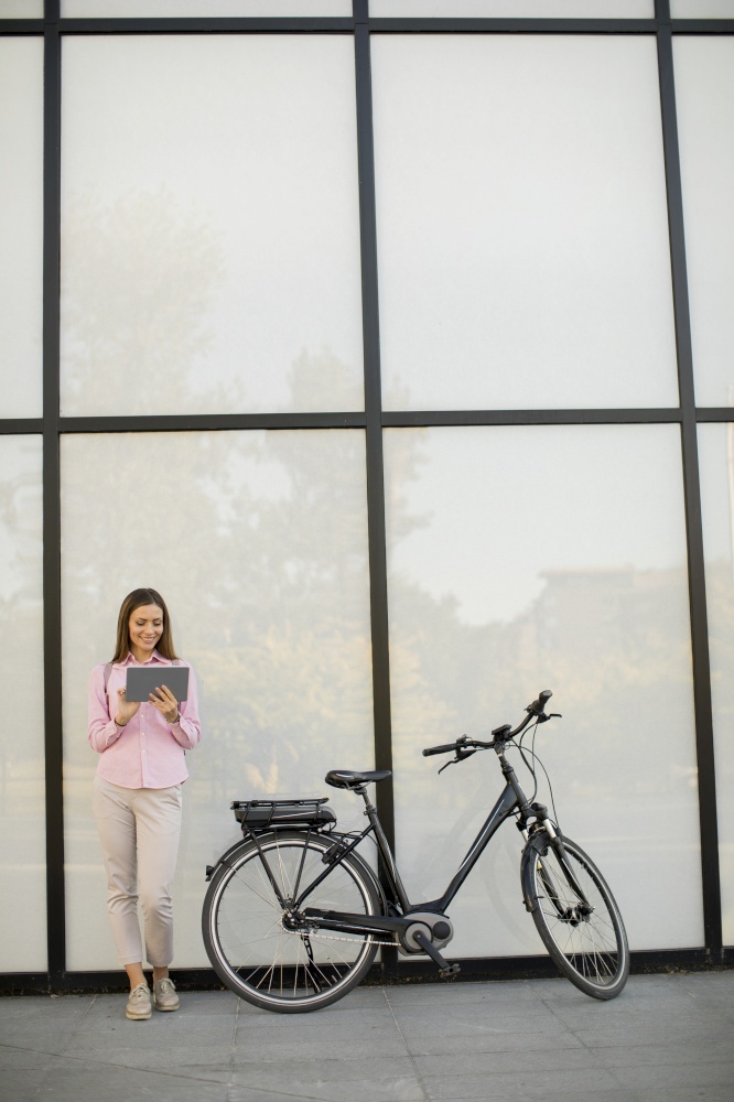 Happy young woman with files in the hands standing outdoor next to electric bike