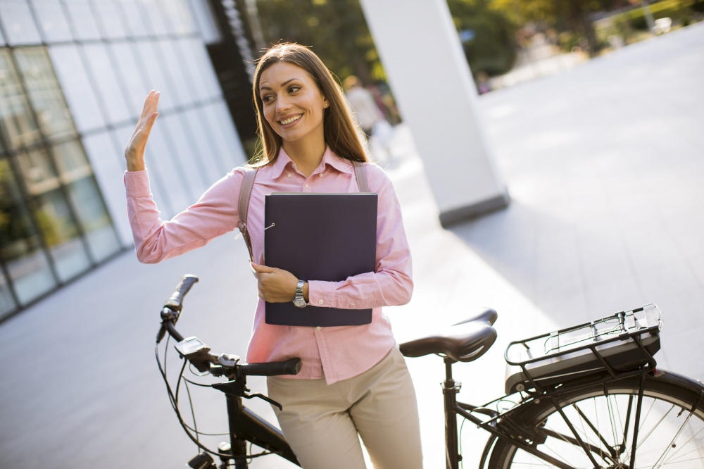 Happy young woman with files in the hands standing outdoor next to electric bike