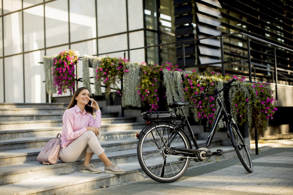 Young woman sitting on the stairs near ebike and usling smartphone outdoor