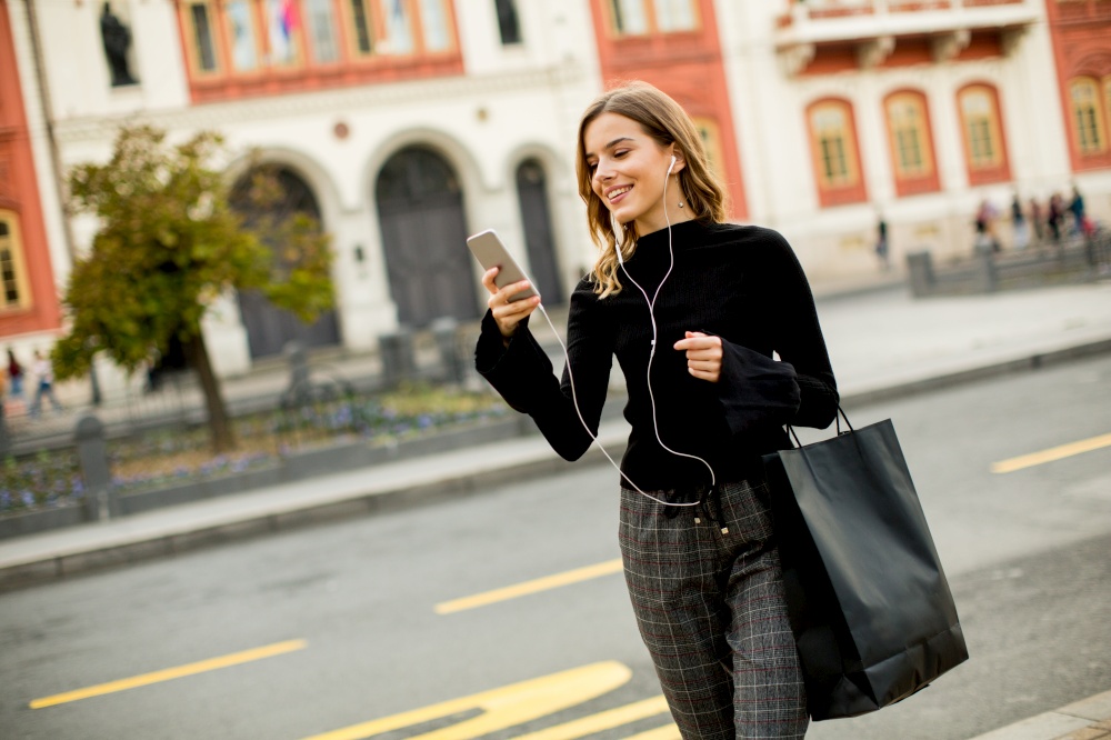 Smiling brunette woman using mobile while standing on street and  waiting for a bus or taxi