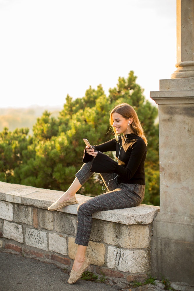 Portrait of young woman holding mobile phone while sitting on the wall