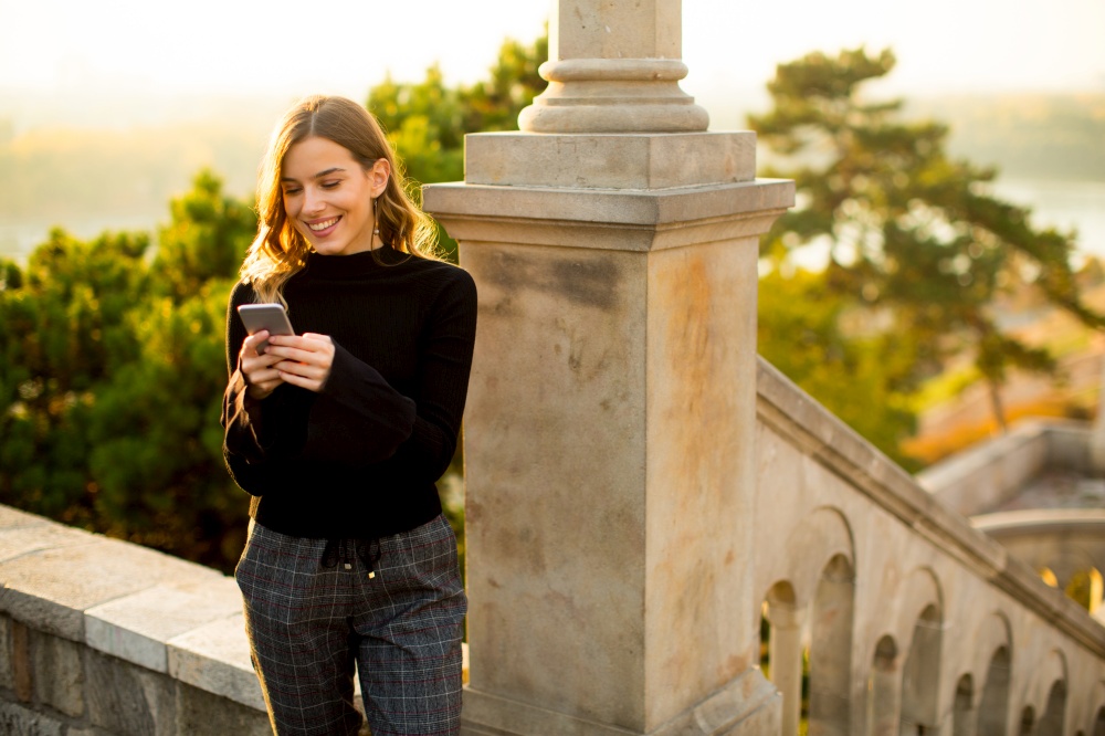 Portrait of young woman holding mobile phone while standing on the old stairs in the park