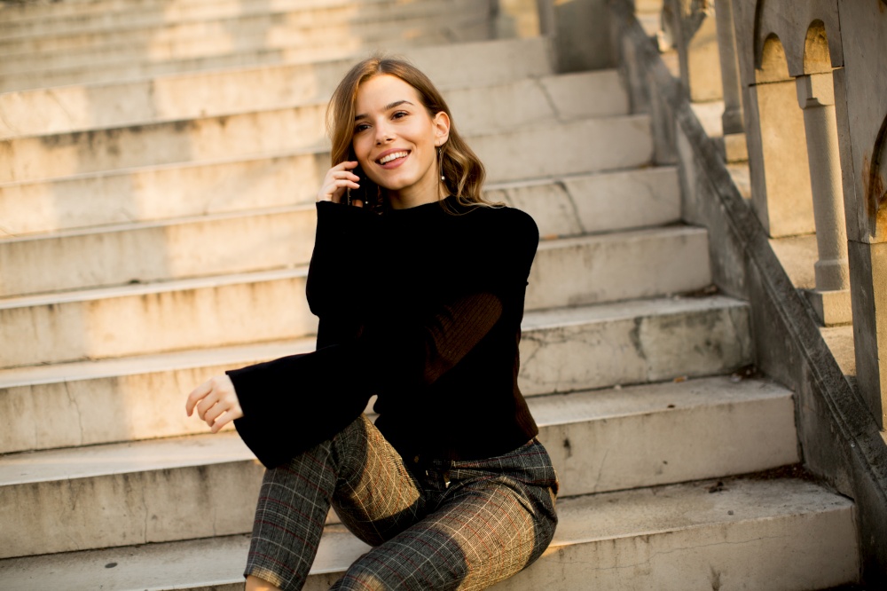 Trendy young woman with mobile phone sitting at stairs outdoor