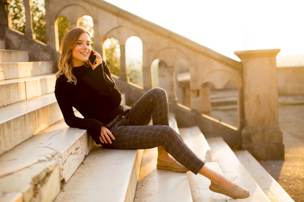Portrait of young woman holding mobile phone while sitting on the stairs outdoor