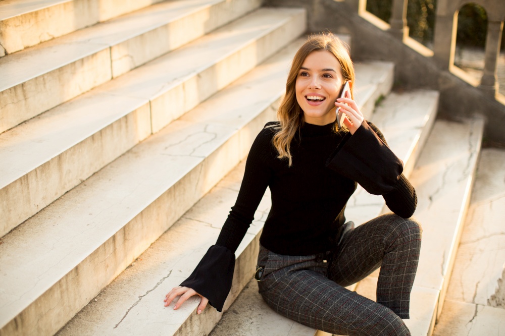 Trendy young woman with mobile phone sitting at stairs outdoor