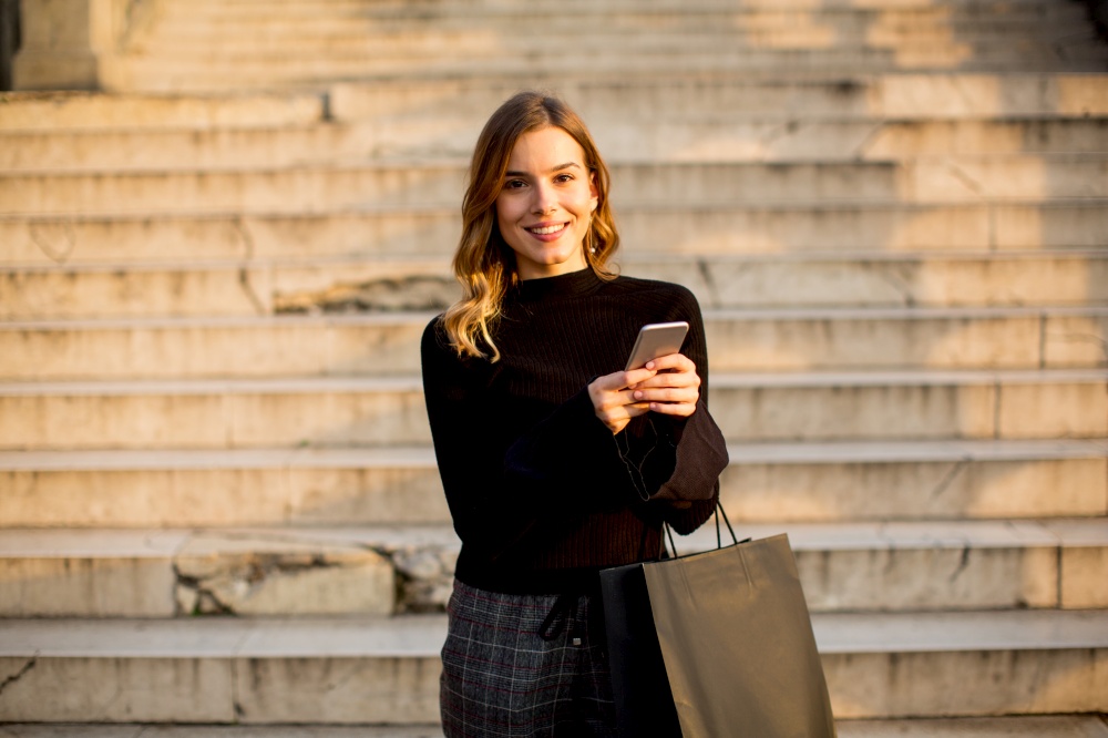 Portrait of young woman with shopping bag and mobile phone outdoor