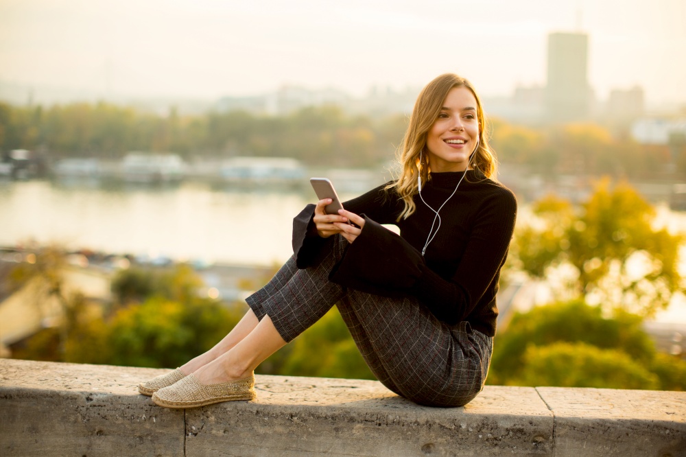Trendy young woman listening music from smartphone outdoor at sunset
