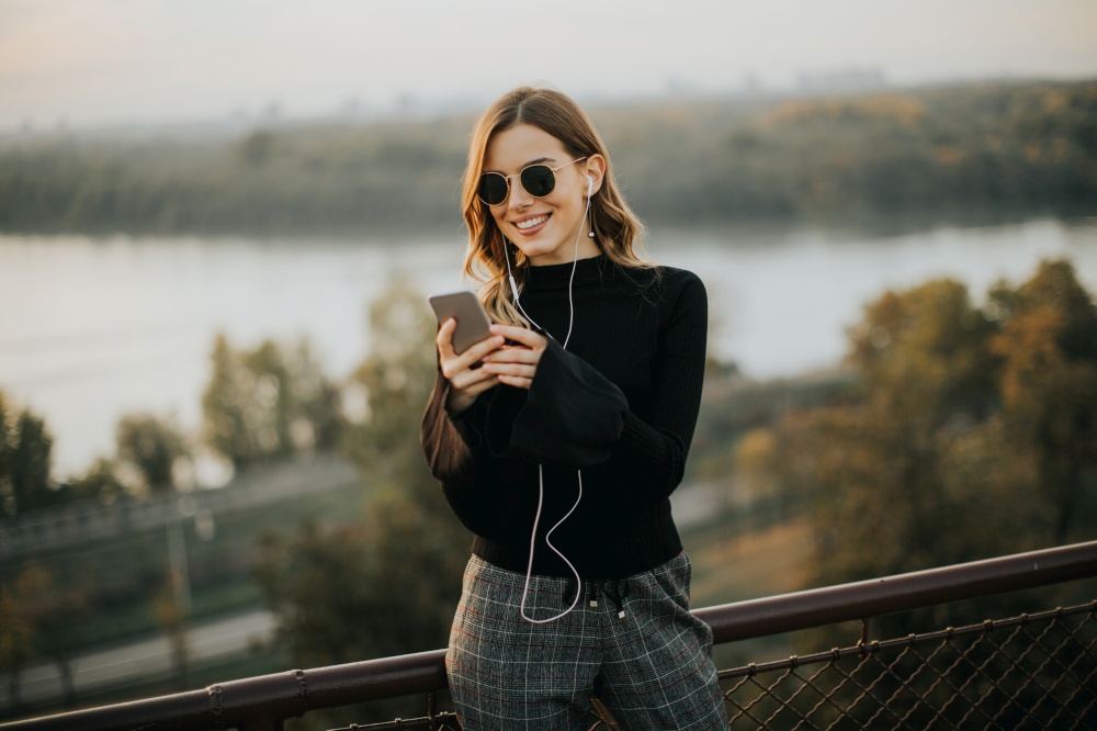 Trendy young woman listening music from smartphone outdoor at sunset