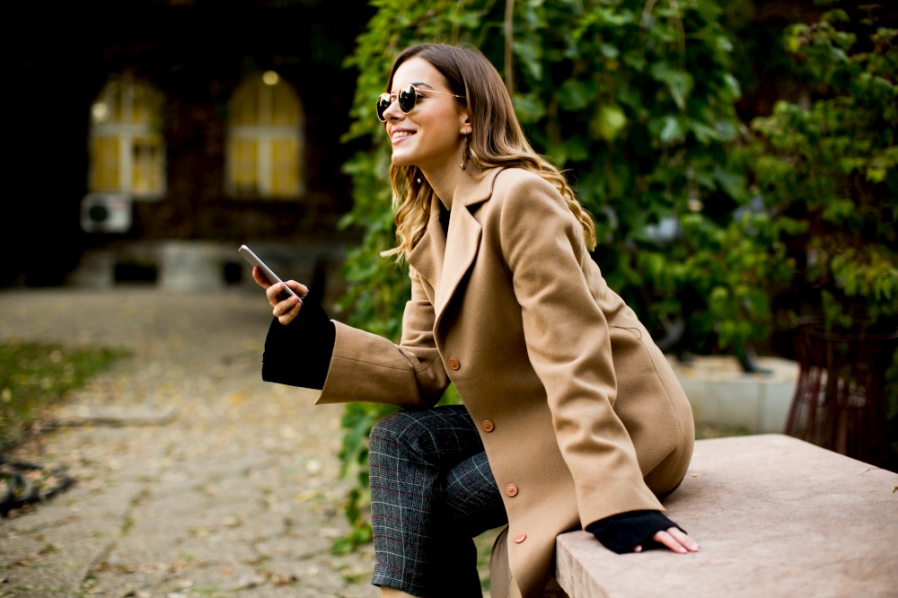 Side view at young woman sitting outdoor and using mobile phone