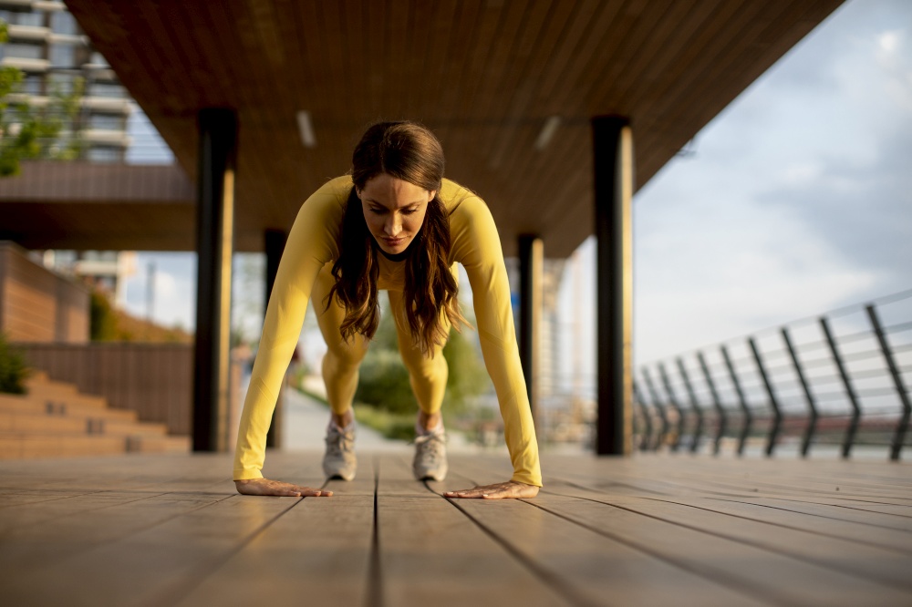 Pretty young woman performing pushups at wooden walkway by the river