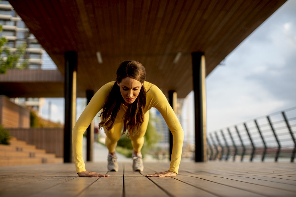 Pretty young woman performing pushups at wooden walkway by the river
