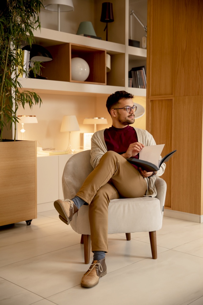 Handsome young man in casual clothes and with eyeglasses reading a book at home