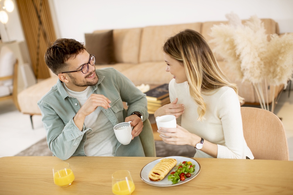 Beautiful young couple talking and smiling while eating healthy  at home.