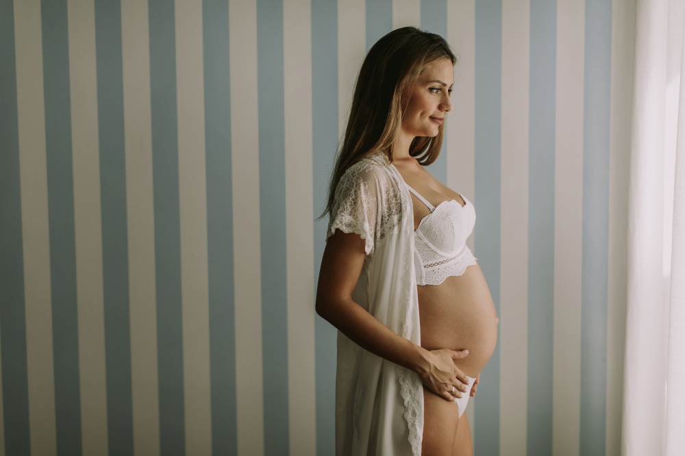 Pretty young pregnant woman standing by the wall in the room