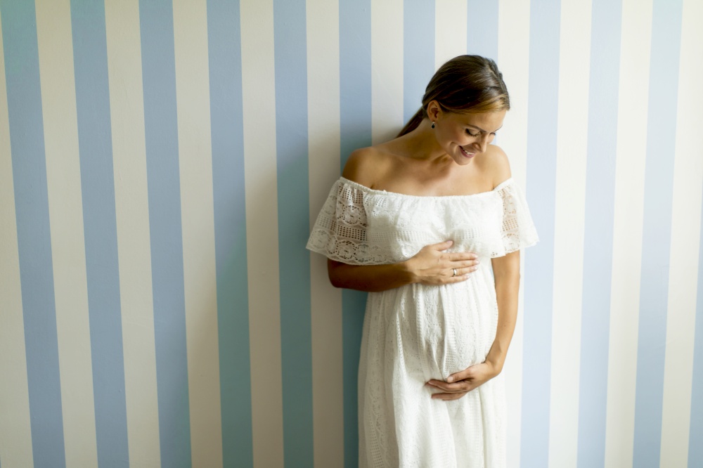 Pretty young pregnant woman standing by the wall in the room