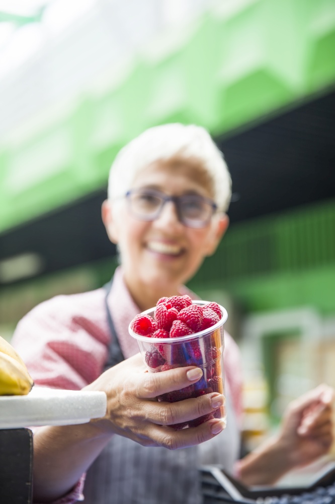 Portrait of senior woman sells raspberries on market