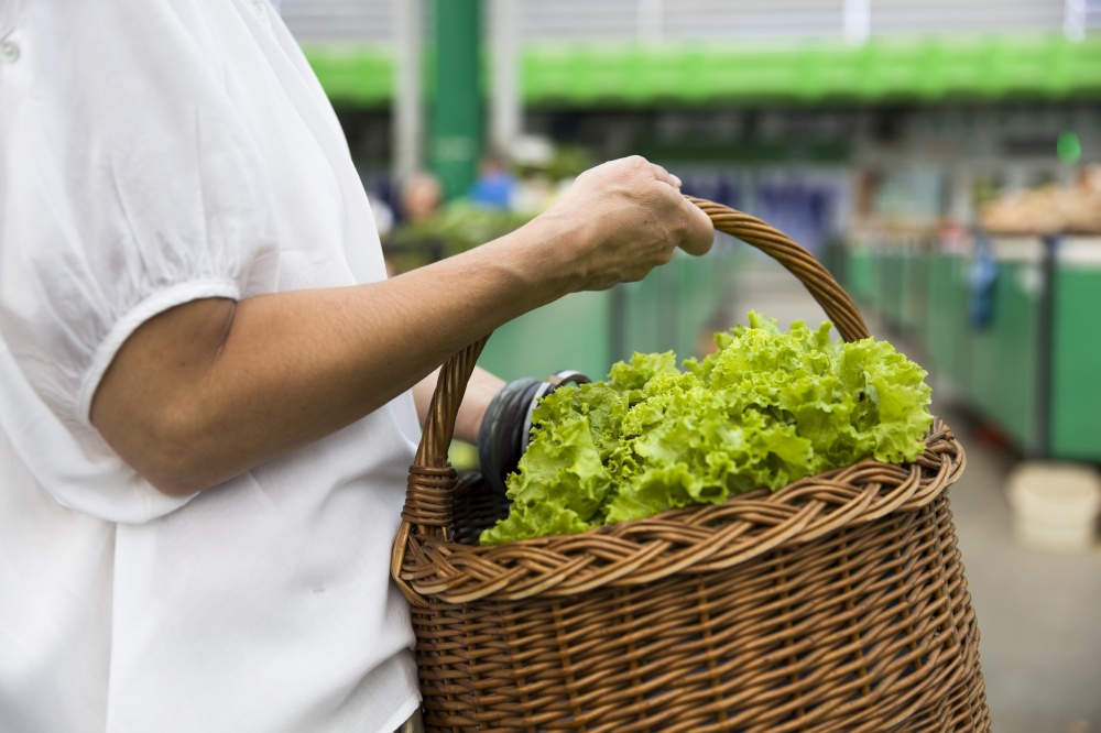 View at senior woman holds basket with lettuce