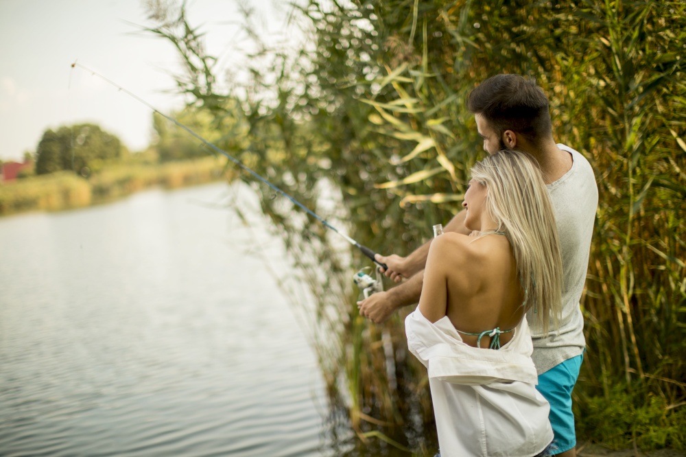 Lovely young couple fishing together by a lake at summer day