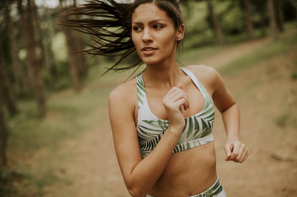 Pretty young fitness woman running at the forest trail