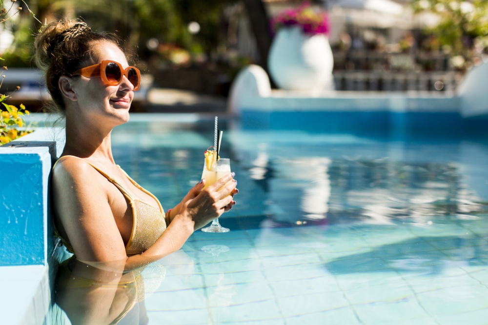 Pretty young woman by the swimming pool with coctail