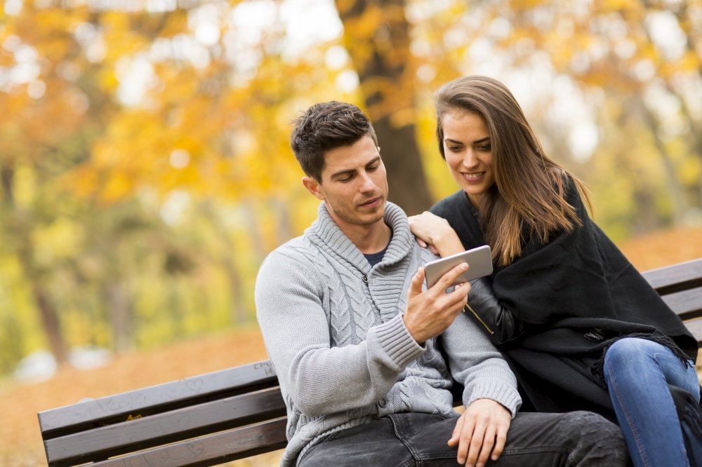 Young smiling couple sitting on bench in autumn park