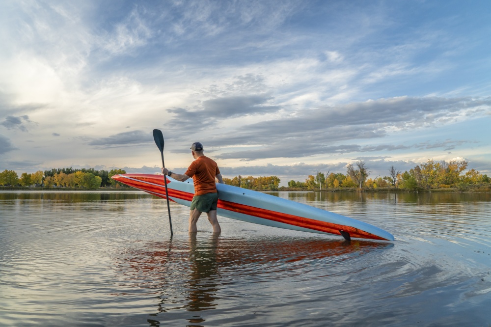 senior male stand up paddler is launching his paddleboard at dusk on a lake in Colorado, fall scenery