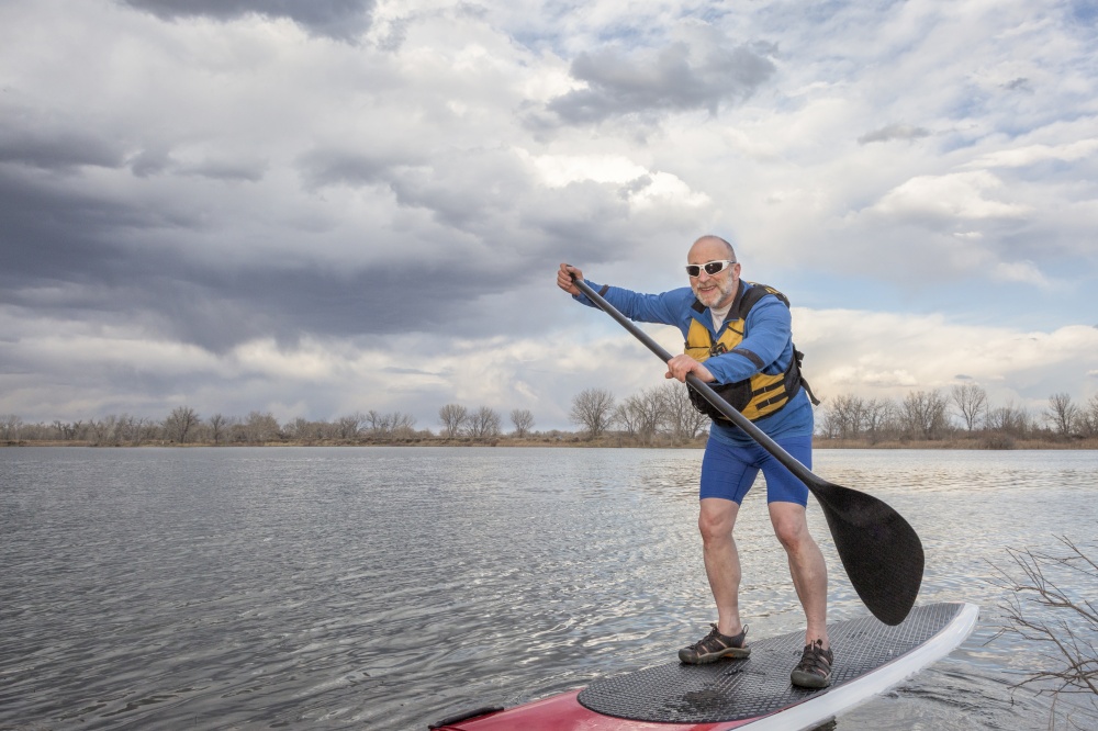 happy senior male paddler on a stand up paddleboard, lake in Colorado in early spring scenery