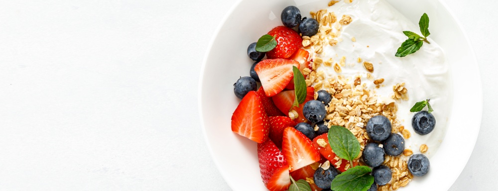Breakfast bowl with granola, plain yogurt, strawberry and blueberry. Top view. Banner