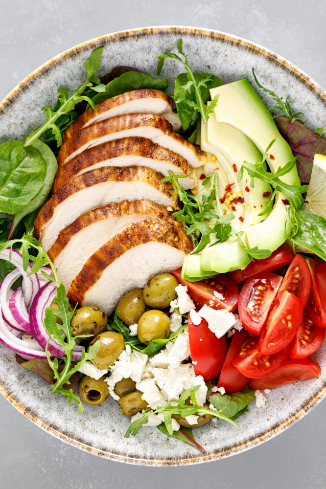 Grilled chicken breast and fresh vegetable salad with tomatoes, feta cheese, olives and avocado. Healthy food. Top view