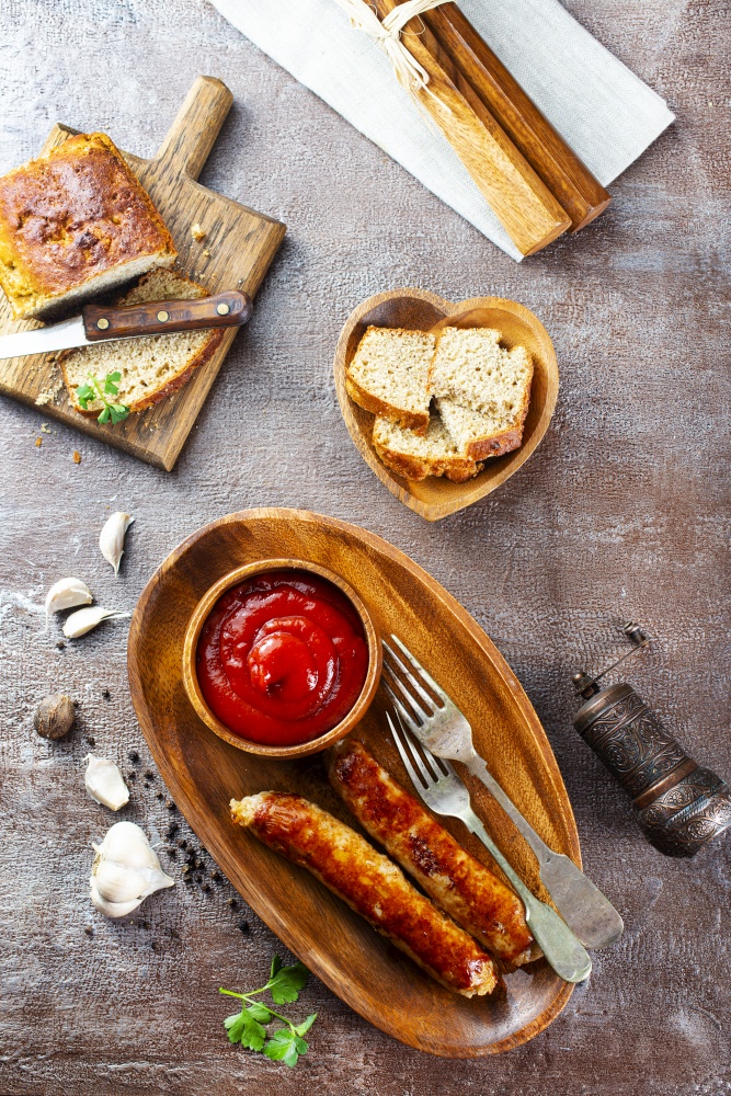 Fried sausages with sauces and herbs on a wooden serving Board. Great beer snack on a dark background. Top view with copy space
