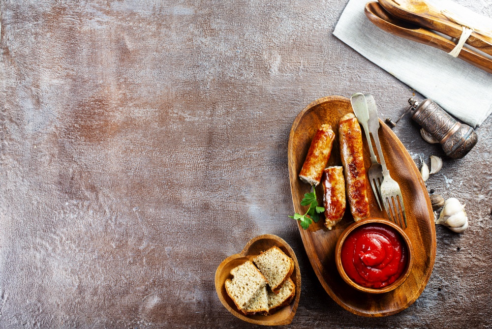 Fried sausages with sauces and herbs on a wooden serving Board. Great beer snack on a dark background. Top view with copy space