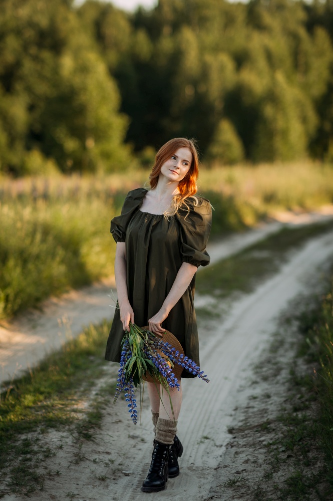 A village red-haired girl walks along a rural road in summer.. Portrait of a village girl on a rural road 3293.