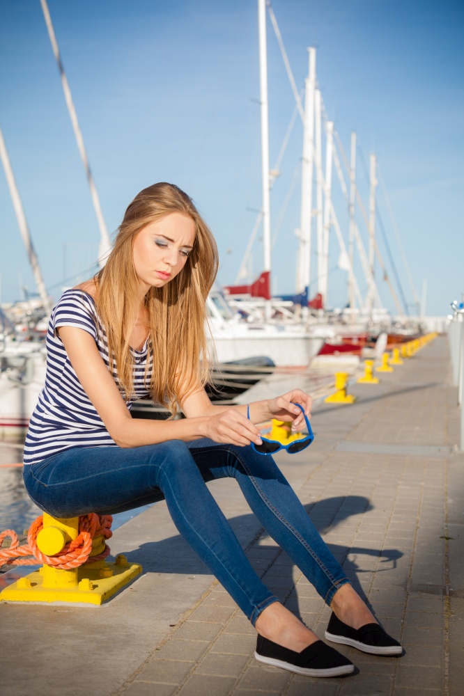 Travel tourism and people concept. Fashion blonde girl with blue heart shaped sunglasses in marina against yachts in port