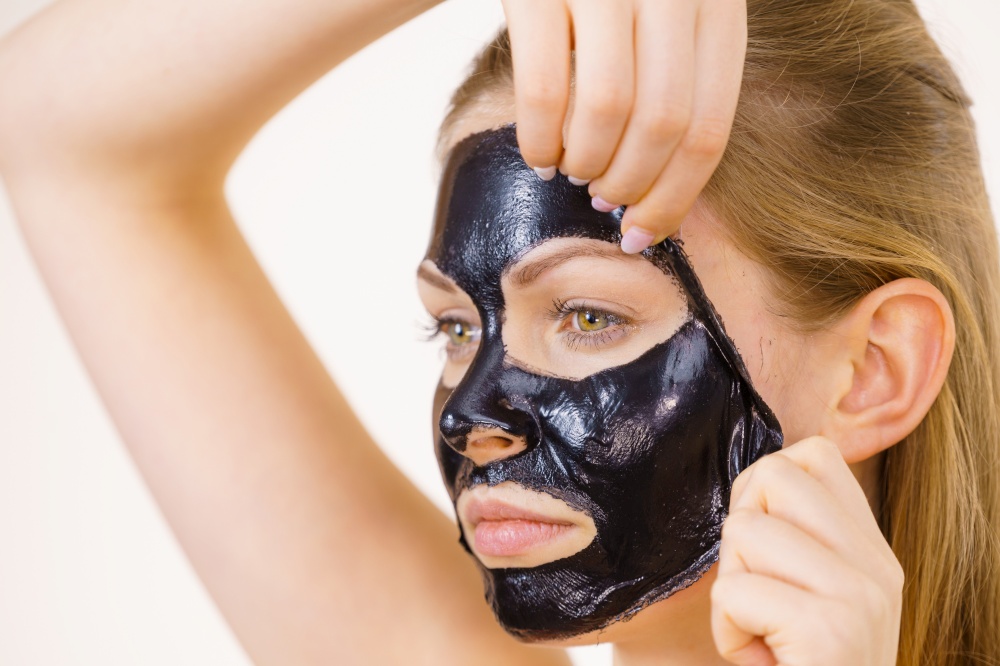 Young woman removing carbo black peel-off mask from her face, on white. Teen girl taking care of oily skin, cleaning the pores. Beauty treatment. Skincare.. Girl removes black mask from face