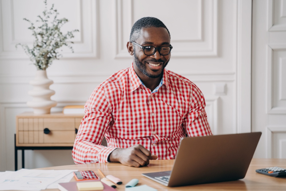 Young happy african american man office worker chatting online with business partner while working on laptop pc, smiling dark skinned entrepreneur enjoying remote work from home. Happy african american man office worker chatting online with business partner via internet