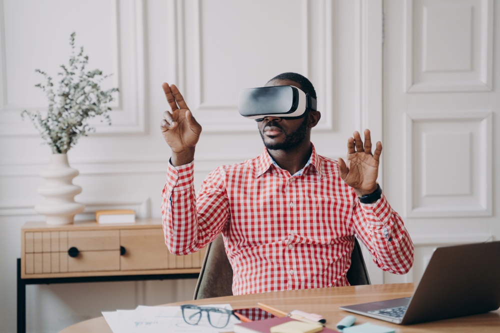 Concentrated Afro American businessman using VR headset, experiencing virtual reality while playing video game. Afro male pointing fingers up seemingly interacting with objects from cyber space world. Concentrated Afro american businessman using VR headset, experiencing virtual reality playing game