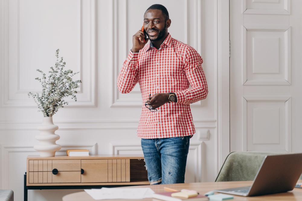 Handsome successful young african businessman in casual clothes enjoying phone call, using modern smartphone at work, smiling afro american guy office worker consulting client via mobile in office. Handsome successful young african businessman in casual clothes enjoying phone call, usingsmartphone