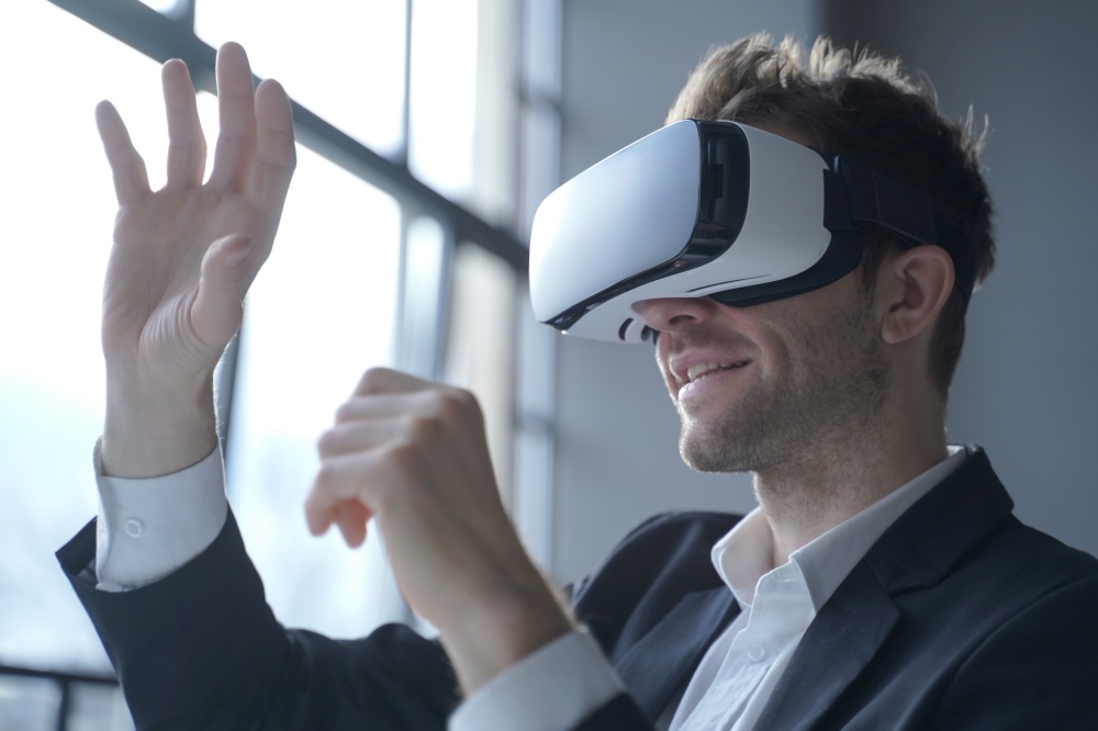 European man office employee wears formal suit and VR headset glasses excited of experiencing virtual reality stretching his hands up trying to catch seemingly round object totally immersed in 3D game. Europian man office employee wears formal suit and VRheadset excited of experiencing virtual reality