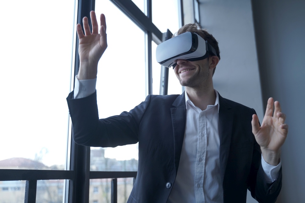 Excited european businessman testing VR glasses at work, using innovative virtual reality technology in business while standing in modern office, happy male employee playing 3d game during break. Excited european businessman testing VR glasses at work, using virtual reality in business