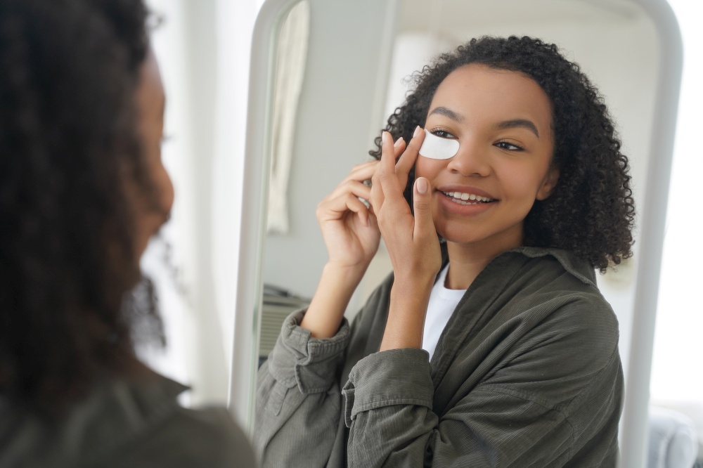 Morning skincare. Happy attractive african american girl is applying eye patch. Skin therapy, moisturizing and nourishing with collagen. Beauty routine and grooming of gorgeous teenage girl.. Morning skincare and beauty routine. Happy attractive african american girl is applying eye patch.