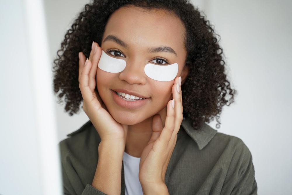 Anti wrinkle procedure. Happy afro girl is applying eye patches. Skin moisturizing and nourishing with collagen. Beauty routine of teenage girl. Morning skincare of young lovely hispanic woman.. Anti wrinkle procedure. Happy afro girl is applying eye patches. Skincare of hispanic young woman.
