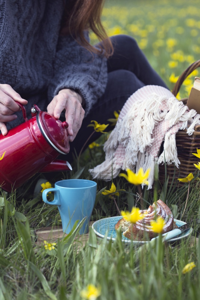 girl pours tea into a cup at the spring picnic in the meadow on the background beautiful wild yellow tulips.