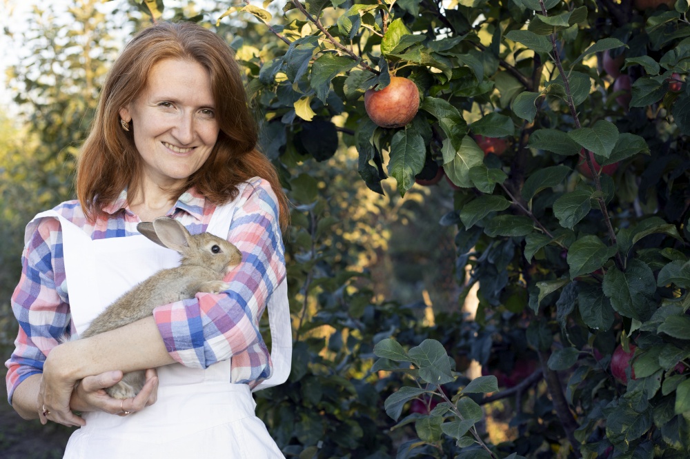 happy girl in the garden holds a rabbit in her arms and a basket of apples nearby. aesthetics of rural life