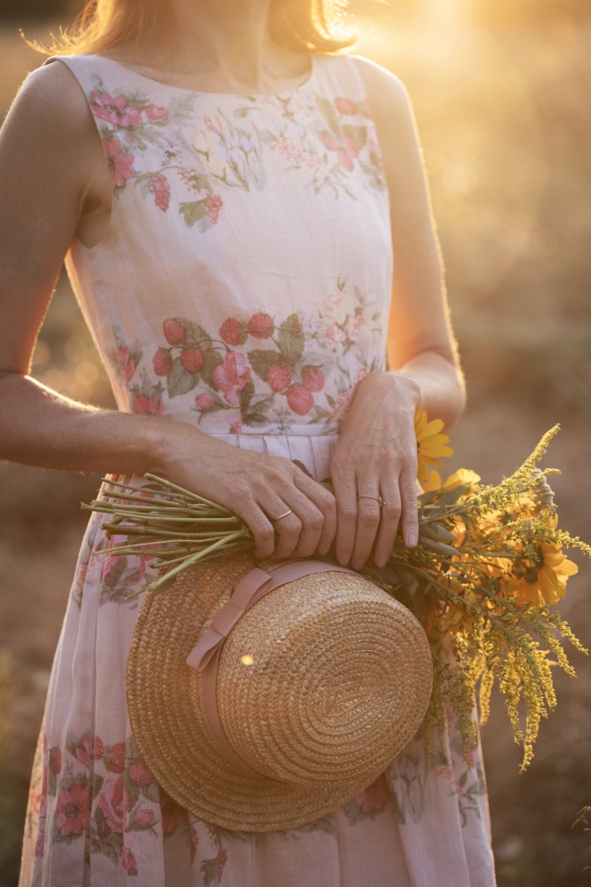 girl in a field at sunset with a hat and a bouquet of wildflowers