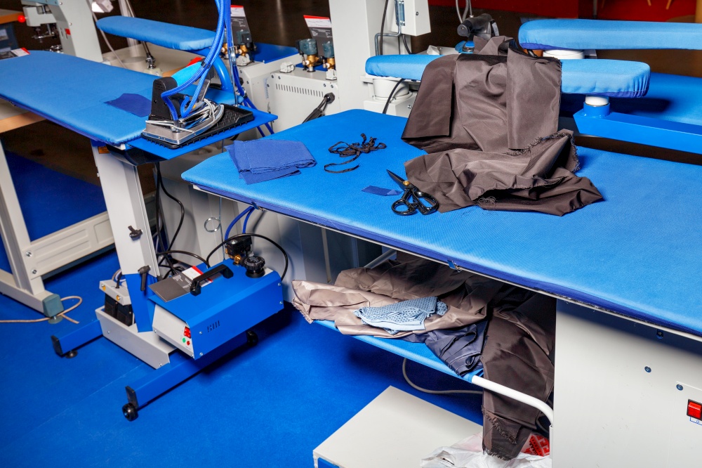 Workplaces of a professional clothes cutter with a steam iron and various fabric cuts.. Professional work tables with blue upholstery fabric of a dress cutter in an atelier studio with a steam iron and various fabrics.
