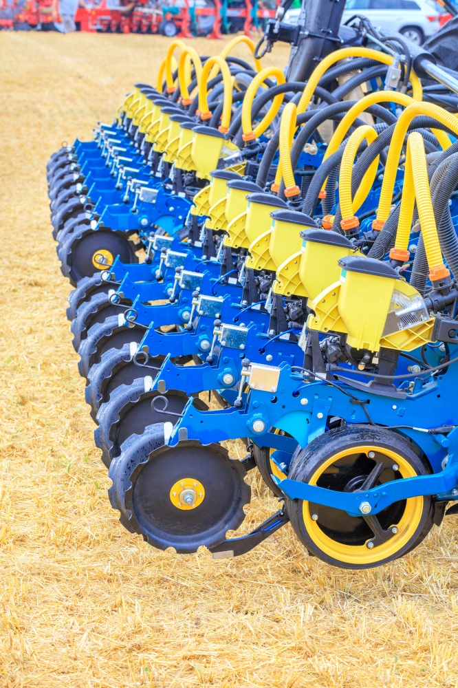 A modern multi row planter and distribution pipes with working mechanisms for pneumatic precise seed distribution against the background of a yellow stubble field. Vertical image. Copy space.. Multi row seeder with a mechanism for precise seed distribution used in agriculture.