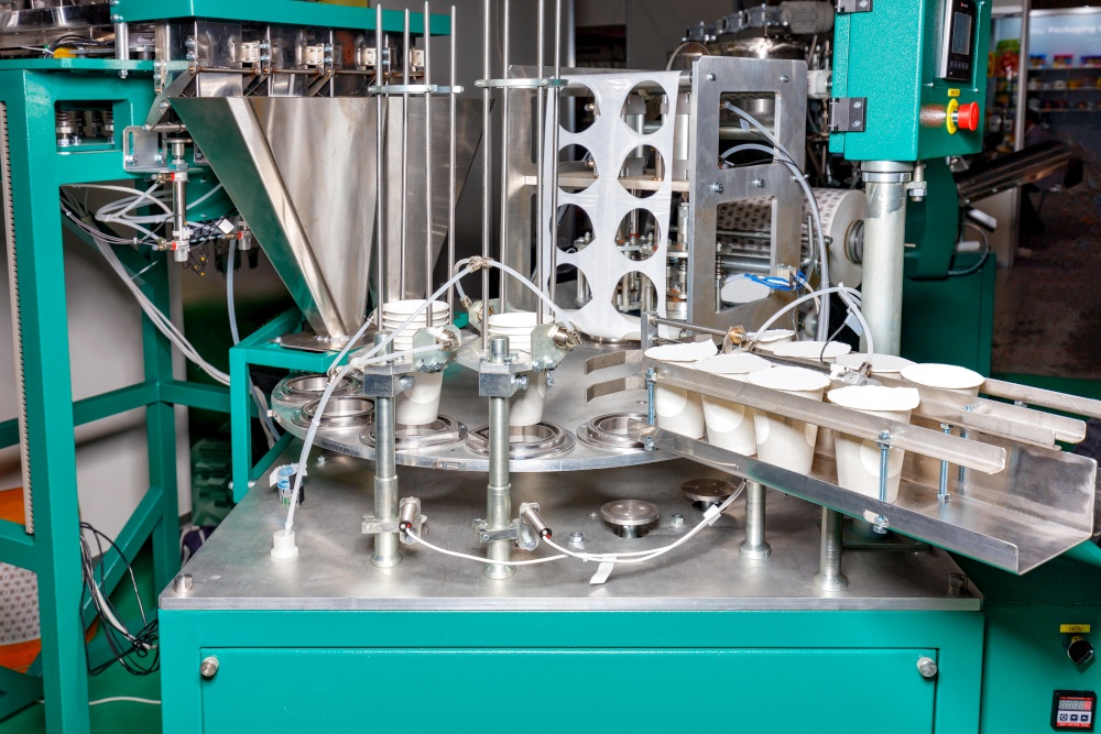 A fragment of an automatic production line for bottling and packaging food liquid yoghurts in paper cups. The concept of processing, storage and packaging of dairy products. Closeup. Copy space.. Production automatic line for bottling and packaging of yoghurts controlled by software.